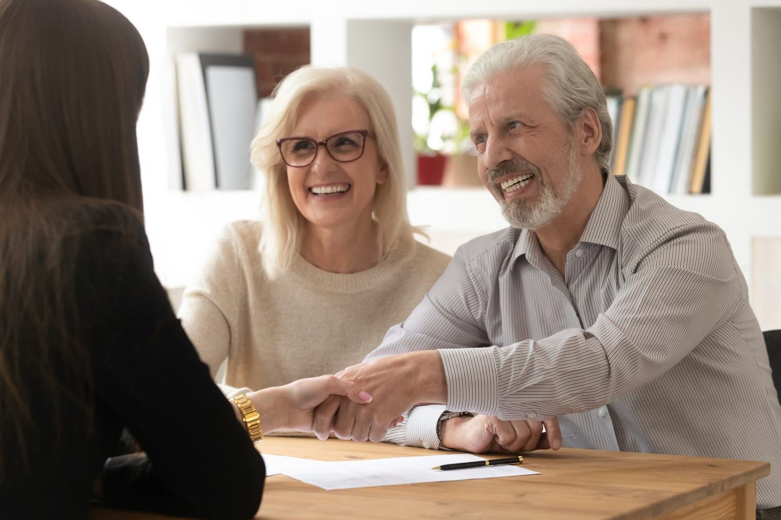 A senior couple smiling as they shake hands with a licensed Medicare agent
